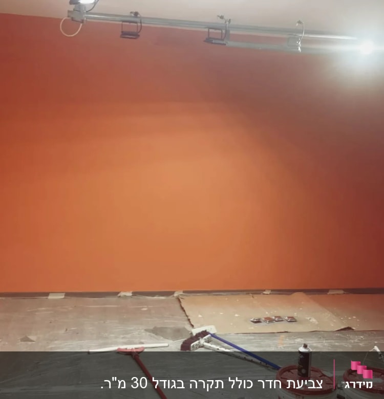 קיר צבוע בכתום עם דליי צבע וכלי עבודה